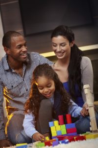 Happy interracial family sitting on floor at home, playing together, smiling.